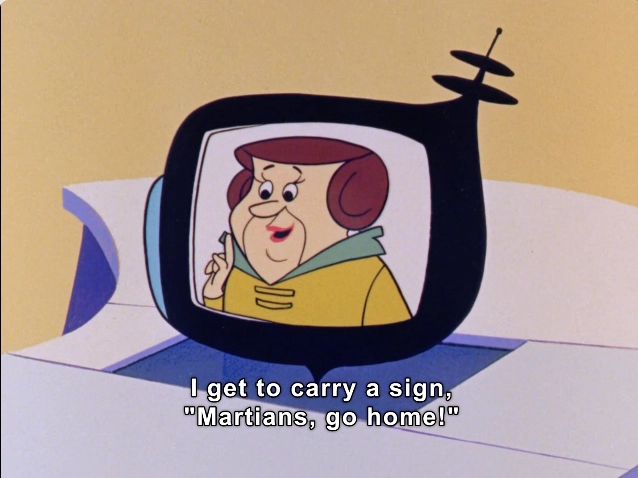 The image features an animated character depicted on a retro-style television screen. The character has a round face with a cheerful expression, wearing earmuffs and a colorful jacket. She appears to be speaking enthusiastically, gesturing with one finger raised. The text below her reads, "I get to carry a sign, 'Martians, go home!'" The background is a bright yellow, adding a whimsical touch to the scene.

#DeportationPlan #ICE #IllegalAliens 