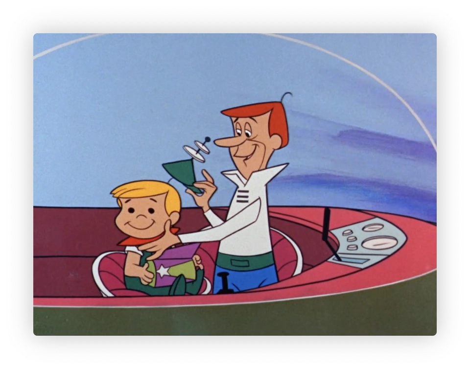 The image shows two animated characters, likely a father and son, from a classic cartoon. They are seated in a futuristic, bubble-top flying car. The father is smiling and holding a green triangular hat while the son, who is holding a small shooting star design lunch box, looks happily at the item. The scene features a simple, stylized sky and horizon in the background, indicating they could be flying or hovering in the vehicle.
