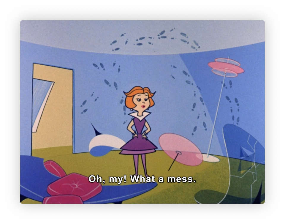 The image shows a scene from an animated cartoon featuring a female character standing in a room with a whimsical design. She appears surprised or dismayed, as indicated by her expression and the caption "Oh, my! What a mess." The room has an abstract and colorful design, with features like a broken chair, scattered petal-like shapes on the floor, and oval pink objects resembling tables or stools. The background includes a large blue wall with a door, and the floor is green, possibly depicting grass. There are surreal elements such as leaves or marks on the walls and a hovering multi-tiered object, adding to the imaginative atmosphere of the setting.