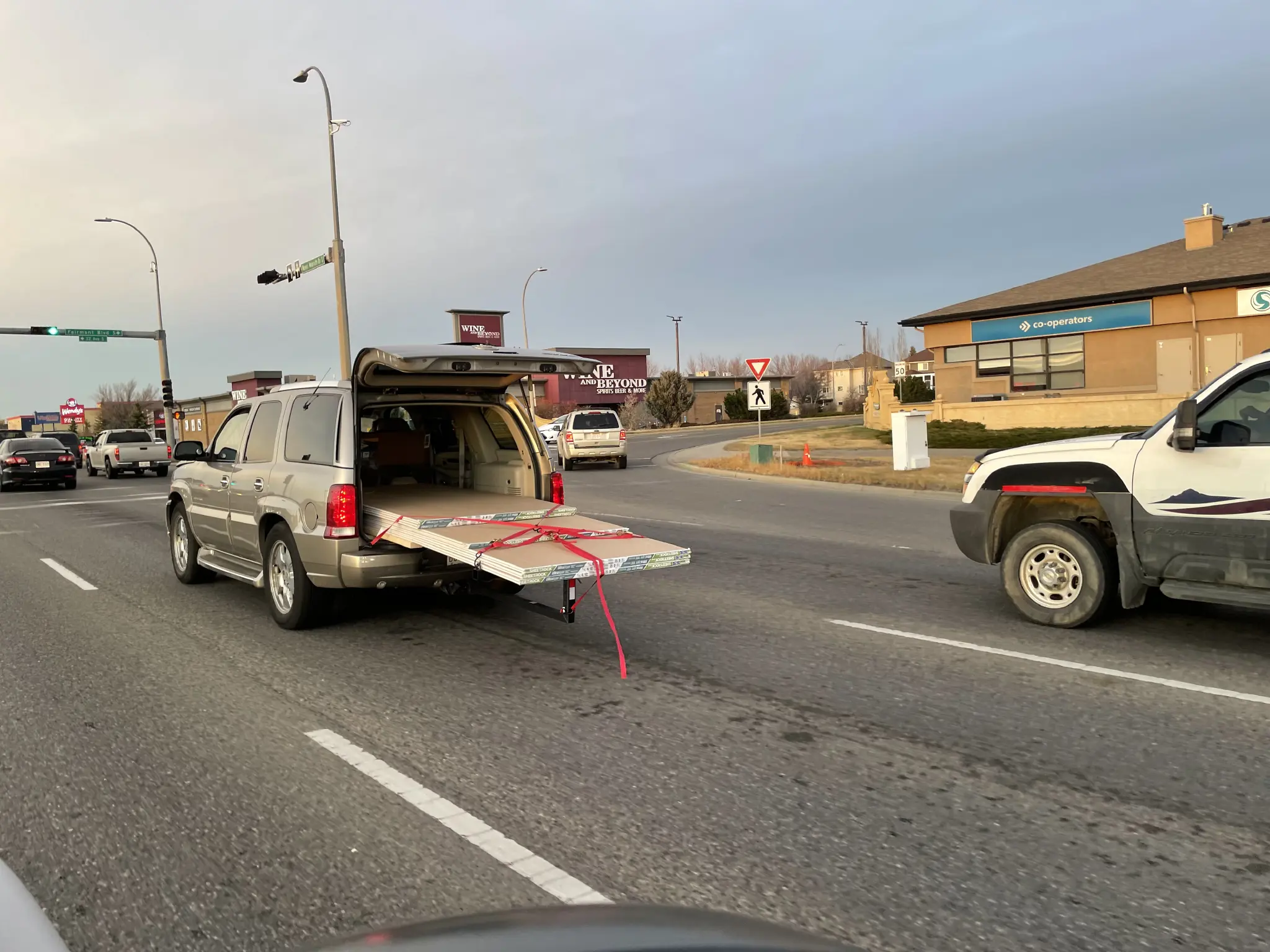 SUV with rear hatch open and long poles of drywall hanging out.
