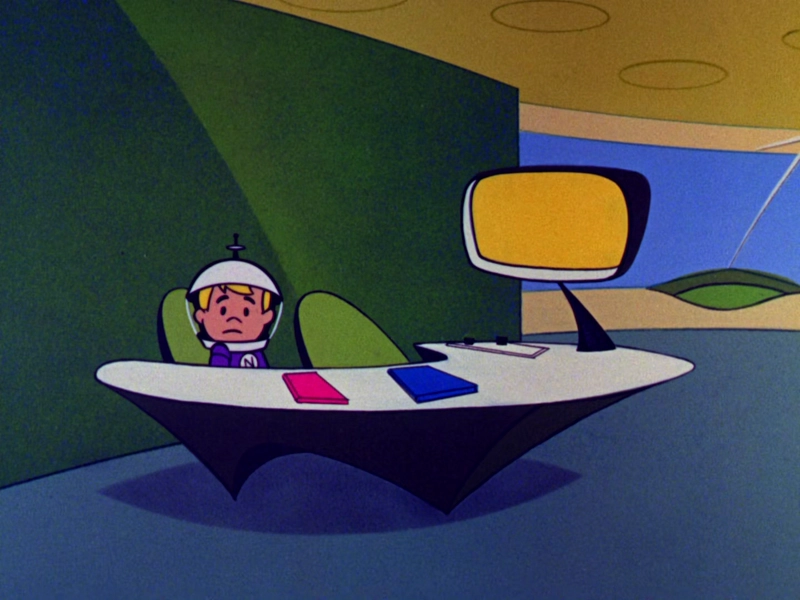 Elroy Jetson, with a space helmet upon his noggin, sits behind a futuristic desk.  He looks to the camera, breaking 4th wall.  He has a sad expression.