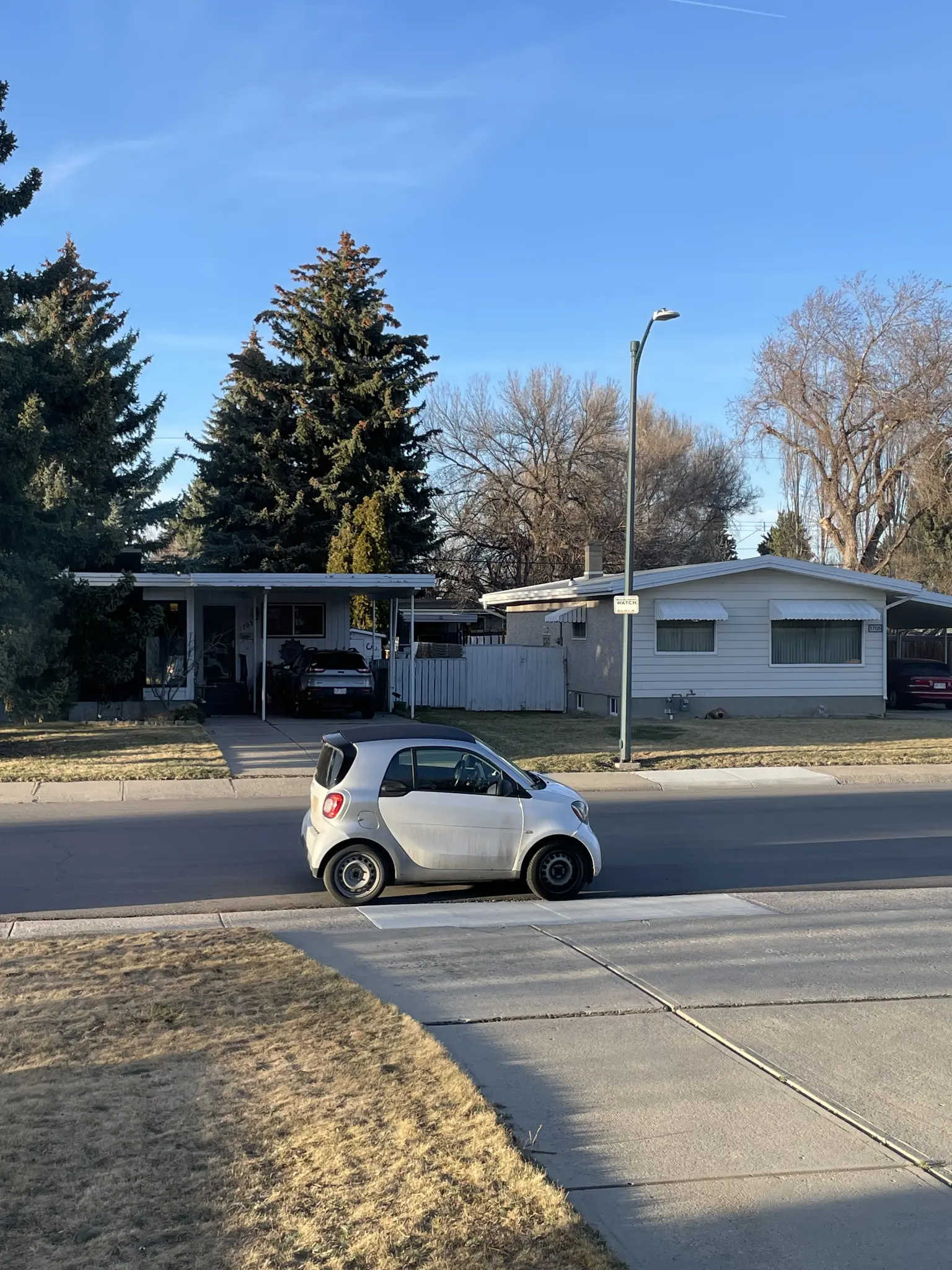 Very small car parked at end of driveway in suburbia.  Might be a fiat 500, not sure. 