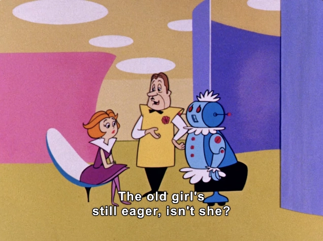 This vibrant animated scene features three characters in a colorful, stylized environment typical of mid-20th century animation. 

On the left, a woman with auburn hair sits in a modern, curved chair, wearing a purple dress. She appears engaged in conversation, her body language suggesting intrigue or curiosity. In the center, a man with a neatly styled haircut and a bright yellow outfit stands confidently, gesturing as he speaks. His expression is animated, hinting at a light-hearted or humorous tone. To the right, a blue, robot-like character stands with a friendly demeanor, adorned with round features and decorative elements, including a frilly collar. 

The text overlay reads, “The old girl's still eager, isn't she?” suggesting a playful banter among the characters. The backdrop consists of soft pastel colors and abstract shapes, contributing to the whimsical, retro-futuristic aesthetic of the scene. This setting evokes a sense of nostalgia, reminiscent of classic animated series t