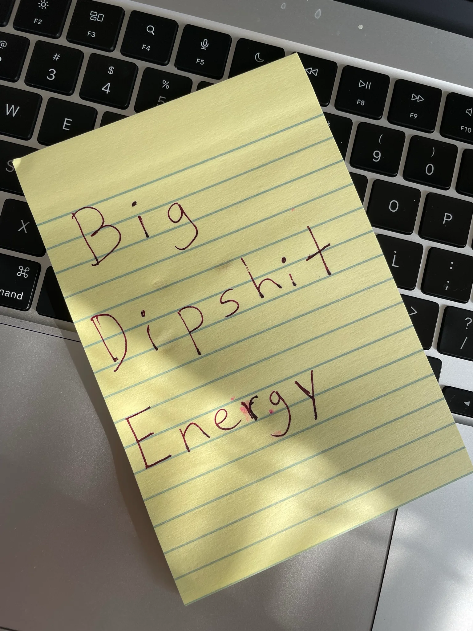 Yellow notepad in laptop keyboard.   Large friendly printing that says

Big
Dipshit
Energy